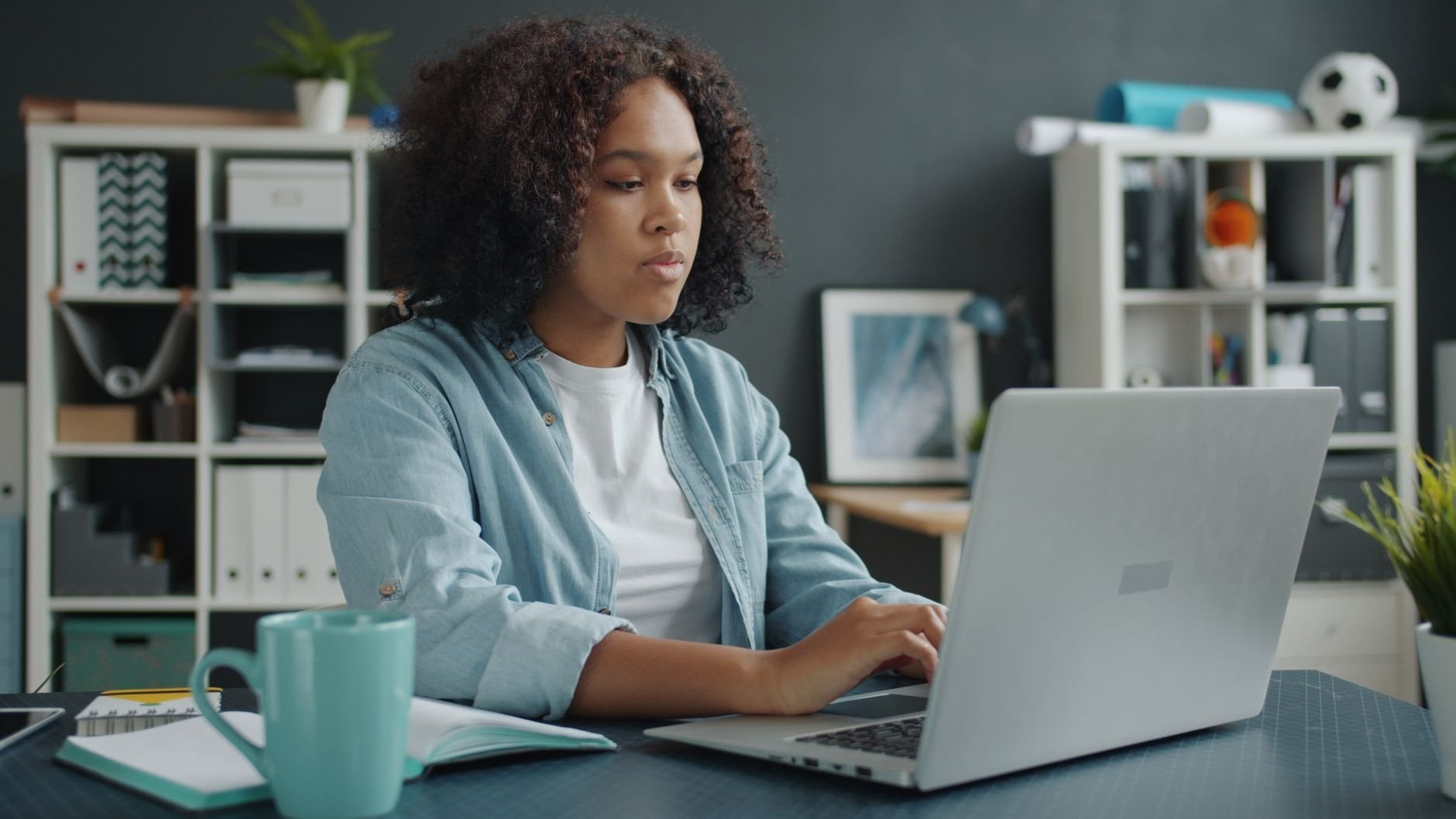 Young woman focused on remote work at home office desk with laptop.